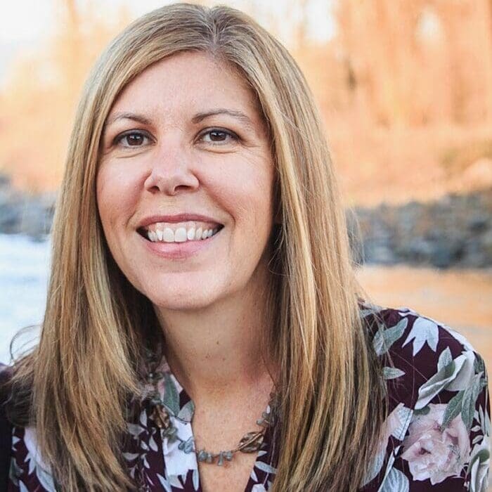 A woman smiling for the camera in front of trees.