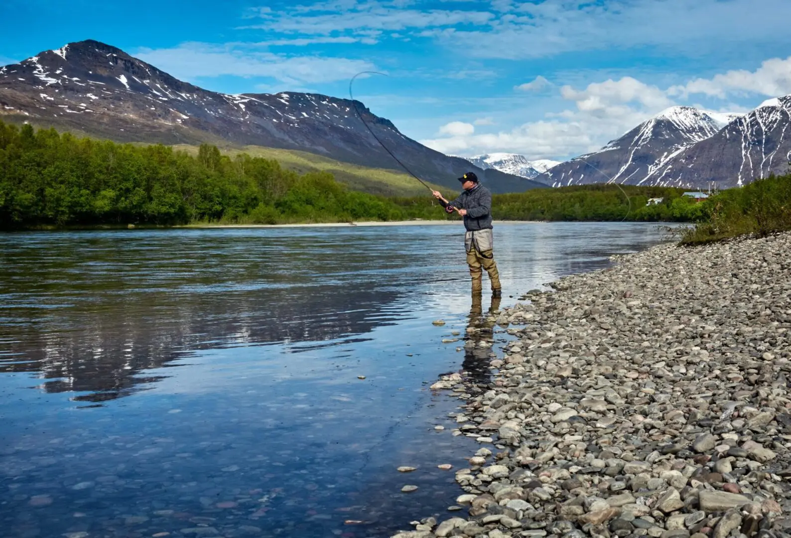 A man standing on the shore of a river fishing.